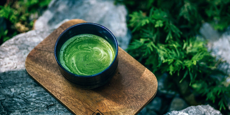 a cup of matcha on a wooden plate on some stones in the forest
