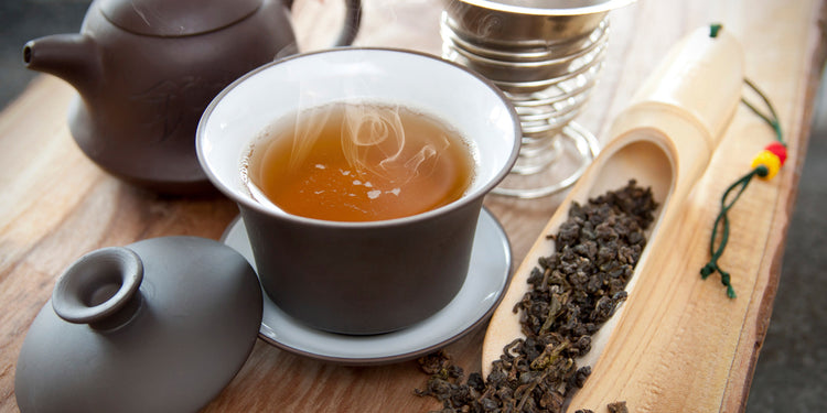 a cup of oolong tea on a wooden board with loose oolong tea